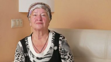 Kadın ciddi görünümlü kameraya yaşlı ve etrafına bakıyor. Evde kanepede dalgın bir kadın portresi