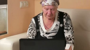 Kadın evde kanepede dizüstü bilgisayar üzerinde çalışan yaşlı. O ekrana bakar ve anahtar presler. İçinde belgili tanımlık akvaryum yüzme balık yanında.