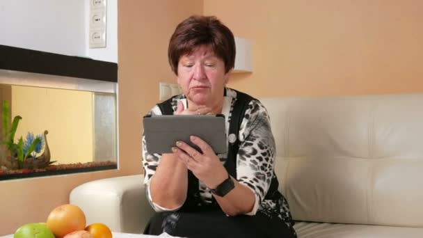 Старшая женщина кашляет и общается с врачом на видеоконференции. Врач на таблетке онлайн дает рекомендации пациенту на дому — стоковое видео