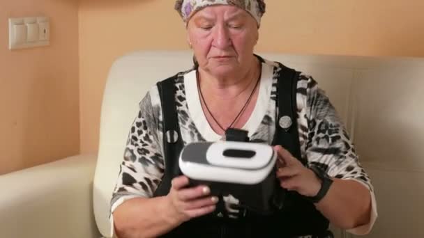 Mulher envelhecida familiarizado com óculos de realidade virtual. Ela traz pontos para a cabeça e reviravoltas em diferentes direções. Mãos a tentar tocar nas coisas invisíveis — Vídeo de Stock