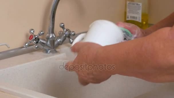 Woman aged washes dishes at home on huhne. She gently wipes the cup and fork sponge. It uses a detergent — Stock Video