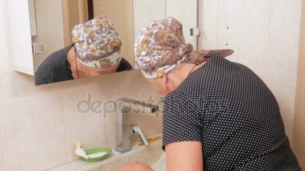 Mujer mayor cepillándose los dientes en el baño. Usted puede ser visto reflejado en una caja de espejo . — Vídeo de stock