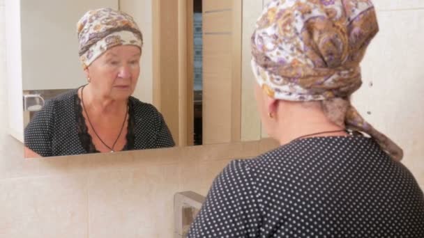 Старшая женщина в ванной применяет антивозрастной лосьон. Вас можно увидеть отраженным в зеркальной коробке . — стоковое видео