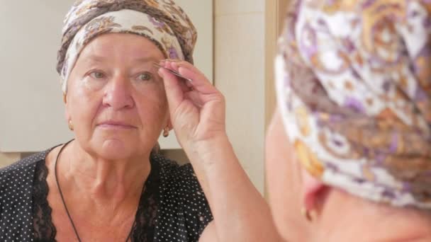 Mulher envelhecida arranca sobrancelhas no banho. Pode ser visto refletido em uma caixa de espelho . — Vídeo de Stock
