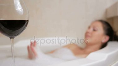 Bir kadeh şarap ile köpük banyosu alarak güzel kız. Bir büyük beyaz banyo ve yüzünde sevinç. gevşeme kavramı