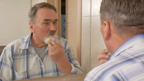 Senior Mann der Rasur im Badezimmer. Es verwendet Rasierschaum und Einmalrasierer. das Konzept der Selbstversorgung — Stockvideo