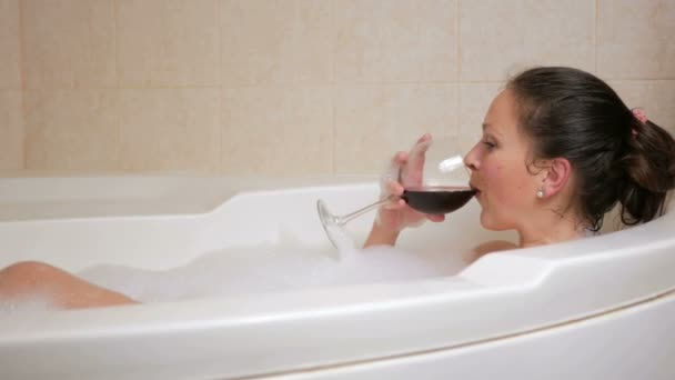 Bella ragazza che fa il bagno con un bicchiere di vino. Un grande bagno bianco e gioia sul suo viso. concetto di rilassamento — Video Stock