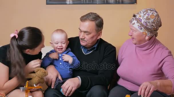 Duży szczęśliwą rodzinę z małym dzieckiem, jej matka, dziadkowie i baw się w domu na kanapie. Śmieją się i mówią między sobą. Pojęcie szczęścia rodzinnego — Wideo stockowe