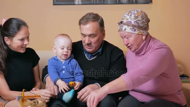 Gran familia feliz con un bebé su madre y sus abuelos se divierten en casa en el sofá. Se ríen y hablan entre ellos. El concepto de felicidad familiar — Vídeo de stock