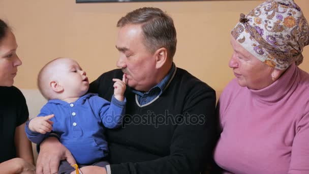 Grande famille heureuse avec un bébé sa mère et ses grands-parents s'amusent à la maison sur le canapé. Ils rient et parlent entre eux. Le concept de bonheur familial — Video