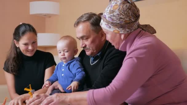 Šťastná rodina s dítětem, její matka a prarodiče bavit doma na gauči. Smát se a mluvit mezi sebou. Koncepce rodinné štěstí — Stock video