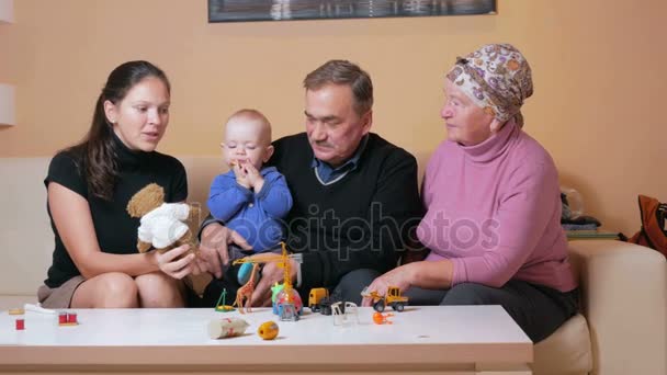Duży szczęśliwą rodzinę z małym dzieckiem, jej matka, dziadkowie i baw się w domu na kanapie. Śmieją się i mówią między sobą. Pojęcie szczęścia rodzinnego — Wideo stockowe