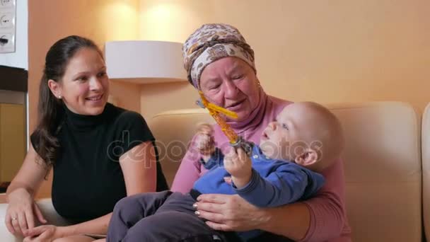 Famille heureuse avec un bébé sa mère et sa grand-mère s'amusent à la maison près de l'aquarium. Ils rient et parlent entre eux. Le concept de bonheur familial — Video