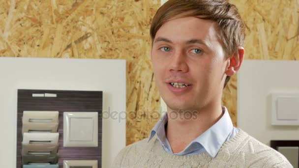 Un joven habla y muestra de interruptores de luz en diferentes colores y formas. Las muestras se presentan de nuevo al stand. Tienda electricistas — Vídeos de Stock