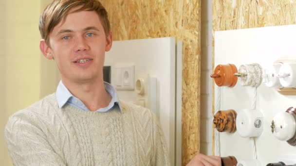 Een jongeman vertelt en toont de schakeloptie sockets en draden van verschillende kleuren en vormen. Monsters worden gepresenteerd op een speciale stand. Kijkend naar de camera — Stockvideo