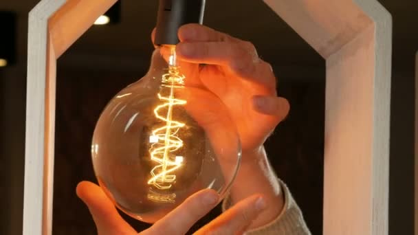 Young man twists Edison bulb in the lamp designer. Vintage lamp with long strands of filament. Beautiful warm light. Close-up — Stock Video