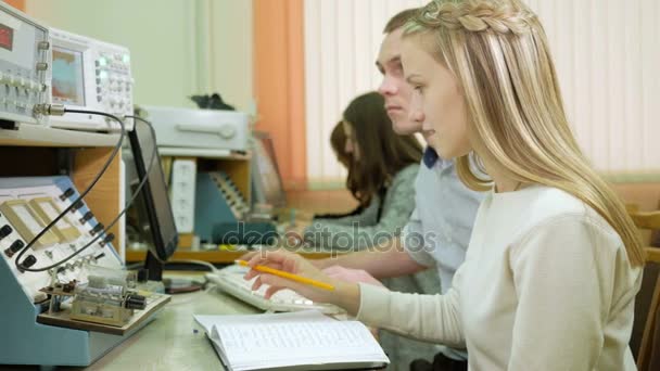 Atractiva joven rubia está estudiando en la universidad como ingeniera. Junto con el joven anotar las lecturas sobre el trabajo de laboratorio . — Vídeo de stock