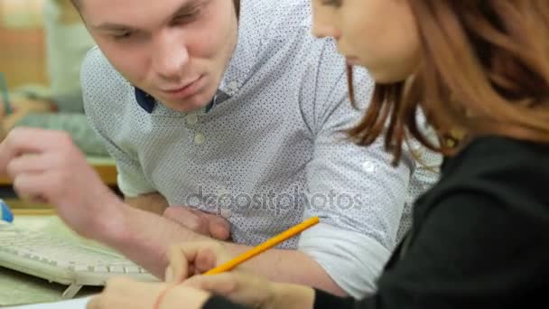 Estudiante masculino aconseja a las mujeres cómo escribir correctamente en un cuaderno algo. Mujer de cabello castaño escribe cuidadosamente bajo el dictado de otro . — Vídeos de Stock