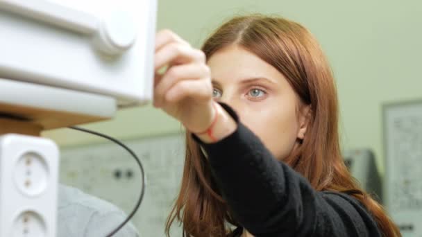 女性エンジニアの学生では、電動発電機を手で調整します。デバイスと兆候を見て慎重に上の数字を変更します。. — ストック動画