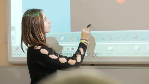 Jovem mulher atraente diz uma aula sobre o fundo de uma placa inteligente. O projetor exibe o elemento da molécula. Ela gira o marcador da molécula — Vídeo de Stock