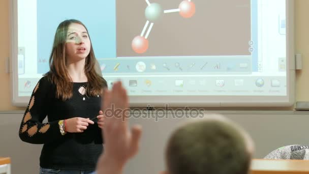 Молода приваблива жінка розповідає лекцію на фоні молекули розумних дощок. Чоловік підняв руку і запитав у вчителя. Вона відповідає на питання . — стокове відео