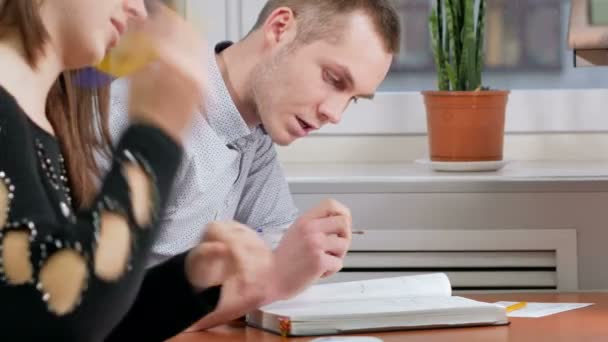 Homme étudiant conseille aux femmes comment écrire correctement dans un cahier quelque chose. Femme aux cheveux bruns écrit soigneusement sous la dictée d'un autre . — Video