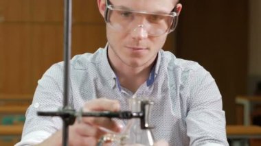 Kimyasallar ve yazar Üniversitesi sonuçlarında ile çalışan genç öğrenci adam. Koruyucu gözlük ve elbisesiz. Şişeler ve şişe sıvı ile.