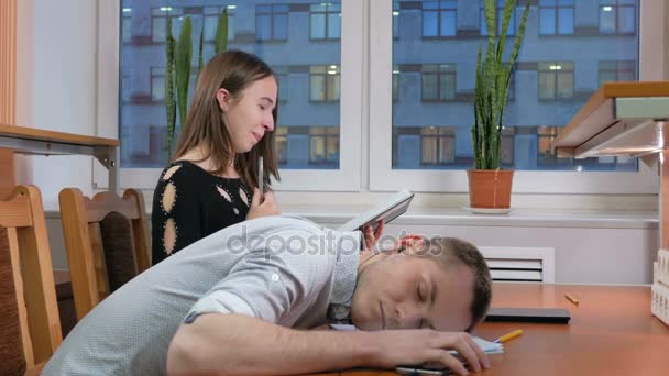 Estudiante cansado durmiendo hombre con auriculares en una conferencia en el cuaderno. Cerca de la mujer registra diligentemente para todos los maestros pluma a papel — Vídeos de Stock