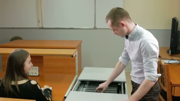 L'homme livre l'université de classe d'ordinateurs portables dans une boîte spéciale. Il sort et met sur la table la femme. Elle fait tourner l'ordinateur. Chargement mobile et chariot de stockage . — Video