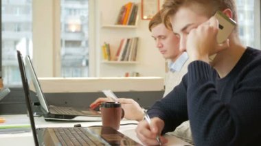 Proje laptoplarda ofiste çalışan genç adam. Bir müşterinin telefonla arıyor ve yanıtları kaydeder. Ekip çalışması kavramı