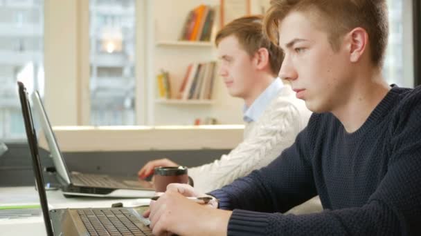 Молодой человек работает в офисе ноутбука над проектом. Сосредоточенно печатают на клавиатуре и смотрят на экран. Концепция командной работы — стоковое видео