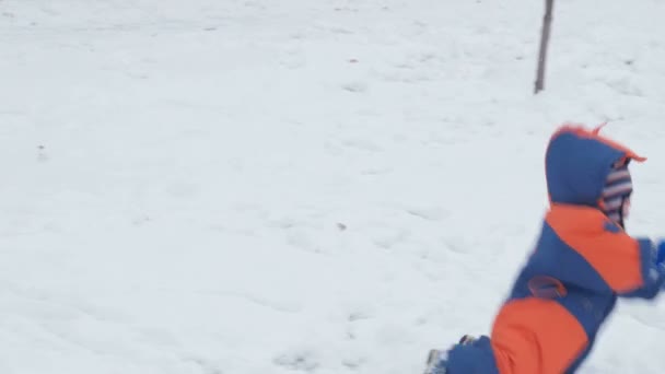 Küçük güzel bebek kar düşüyor. Anne oğlu yükselmeye yardımcı olur. Sıcak tulum, giymiş çocuk bir yıl oldu. Kavram Kış etkinliği — Stok video