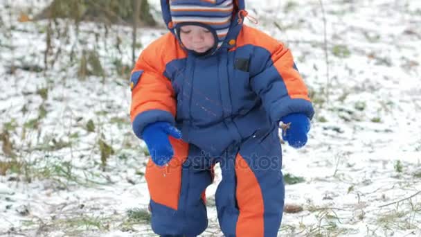 魅力的な赤ちゃんが母親と冬の森で遊ぶ。地上では、雪のビット。サーベルと枝で遊ぶ少年。温かみのあるブルーとオレンジのジャンプ スーツ — ストック動画