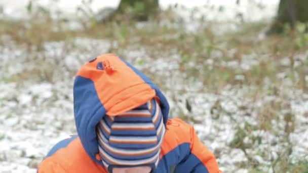 Attraktiva baby spelar i vinter skogen med sin mamma. På marken, lite snö. Pojke leker med sablar och grenar. Varma blå och orangea overallen — Stockvideo