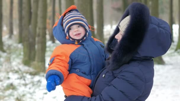 冬に母親の腕の中の魅力的な赤ちゃん。彼らが話すし、笑います。両方は、温かみのあるブルーとオレンジ色の服を着ています。冬の家族旅行のコンセプト — ストック動画