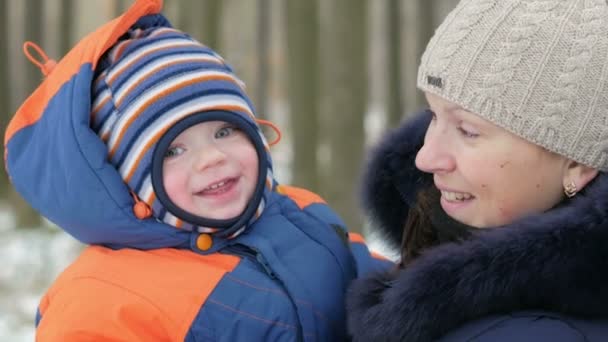 Retrato Bebê atraente em seus braços mães no inverno. Eles falam e riem. Ambos estão vestidos de azul quente e laranja. O conceito de férias em família no inverno. Close-up — Vídeo de Stock