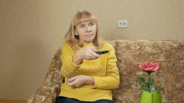 Kadın yaşlı uzaktan kumanda Tv kanalları evde kanepede geçer. Zor bir günün ardından dinleniyor. tatil kavramı