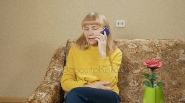 Yaşlı kadın evde kanepede bir cep telefonunda söz. kamera hareketli