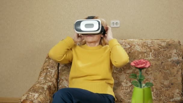 Senior kvinde bærer briller af virtual reality og ser en film. Hun ser sig omkring og vil røre ved de virtuelle vægge. feriebolig koncept – Stock-video