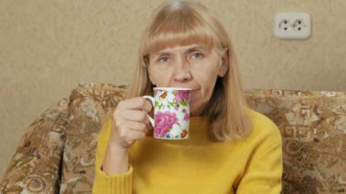 Kadın evde kanepede bir fincan sıcak bir içecek içme ve kameraya bakarak yaşında. Zor bir günün ardından dinleniyor. tatil kavramı