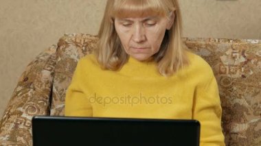 Kadın dikkatle bir dizüstü evde kanepede kabilelerini yaşlı. O klavyede yazarak ve ekrana bakarak. Çalışma evde kavramının