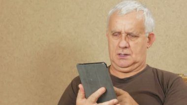 Tablet yaşta adam evde kanepede haberlerde okur. O parmak yapraklar olduğunu sayfaları ilginç değil. tatil ev concept