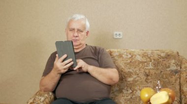 Tablet yaşta adam evde kanepede haberlerde okur. O parmak yapraklar olduğunu sayfaları ilginç değil. tatil ev concept