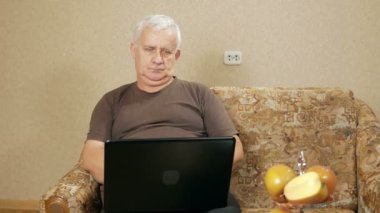 Adam kanepede bir dizüstü bilgisayar, ev çalışma yaşında. Hem elleri ve yazılı çekleri ile dikkatli bir şekilde yazıyor. Ev çalışma kavramı