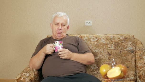 L'uomo all'eta 'di bere caffe' da una tazza e guardare la telecamera. Si rilassa a casa sul divano dopo una dura giornata. concetto di casa vacanza — Video Stock