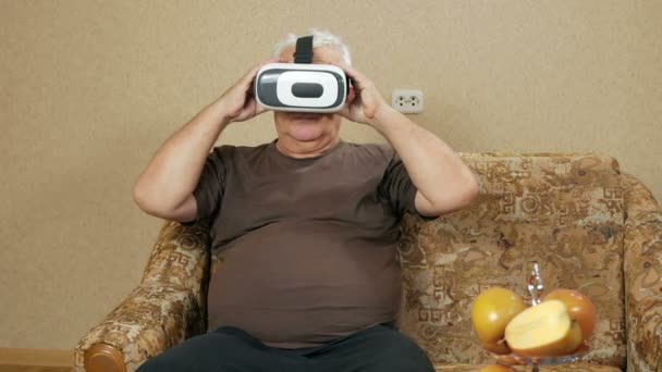 Ο άνθρωπος φοράει γυαλιά στην ηλικία της εικονικής πραγματικότητας στο σπίτι στον καναπέ. Ο ίδιος wags το κεφάλι του και θέλει να αγγίξει τα χέρια του τι συμβαίνει. Μελλοντική τεχνολογία έννοια — Αρχείο Βίντεο