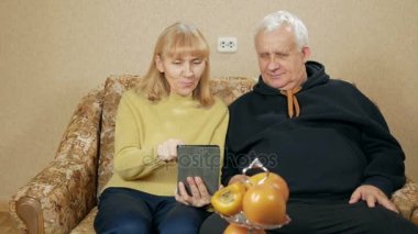 Dijital tablet tutarak ve oturma odasında kanepede otururken gülümseyen kıdemli çift portresi