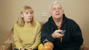 Evde kanepede televizyon izlerken yaşlı bir çift. Kadın gülüyor Tv uzaktan kumanda alır ve ilginç programları seçin. tatil ev concept