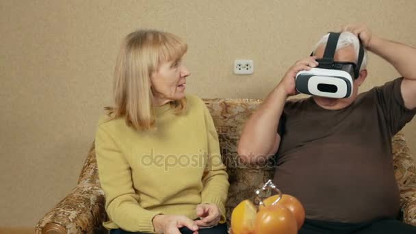 Couple âgé essaie lunettes réalité virtuelle à la maison. L'homme porte des lunettes et ils rient de ce qui se passe. concept de haute technologie — Video