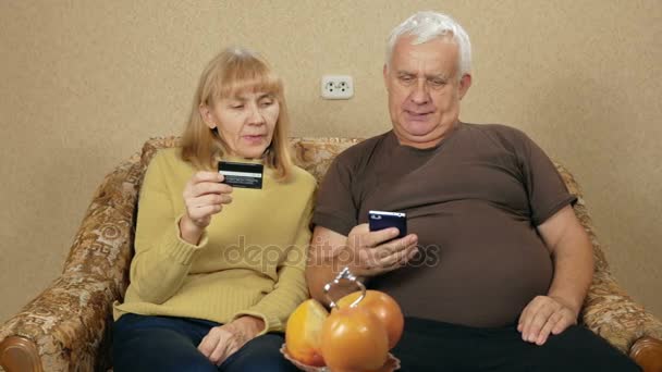 Старший пара оплачувати покупки в Інтернеті за допомогою кредитної картки банку. Жінка диктує число, людина входить інформація в телефон. — стокове відео